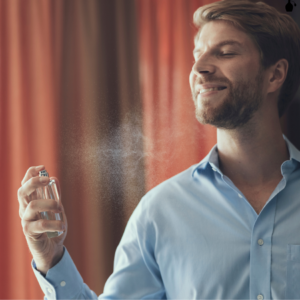 : A man in a light blue shirt smiling while spraying fragrance on himself.