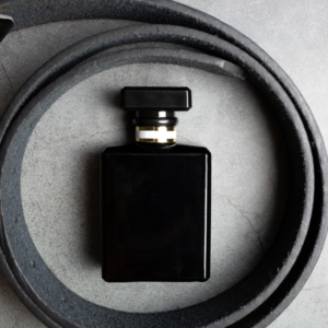 A sleek black bottle of men's fragrance surrounded by a coiled black belt on a grey surface.