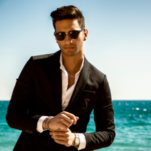 "Confident man in a suit and sunglasses by the beach."