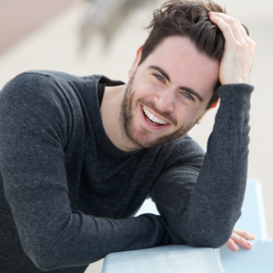 "Smiling man with well-groomed hair and beard touching his hair."