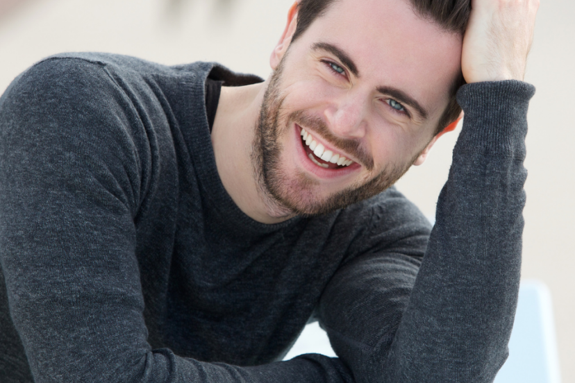 "Smiling man with well-groomed hair and beard touching his hair."